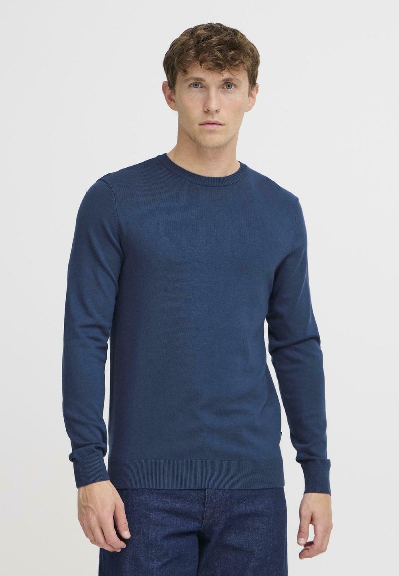 Pulover tricotat bleumarin, cu gât circular, mâneci lungi și manșete cu margine ondulată. Fabricat dintr-un material texturat, cu o formă ajustată.