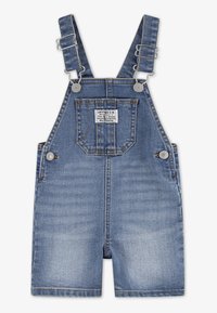 Τζιν σαλοπέτα με ρυθμιζόμενους ιμάντες, μπλε πλύση, με μπροστινή τσέπη και μεταλλικά εξαρτήματα. Φθαρμένες περιοχές προσθέτουν υφή στο ύφασμα.