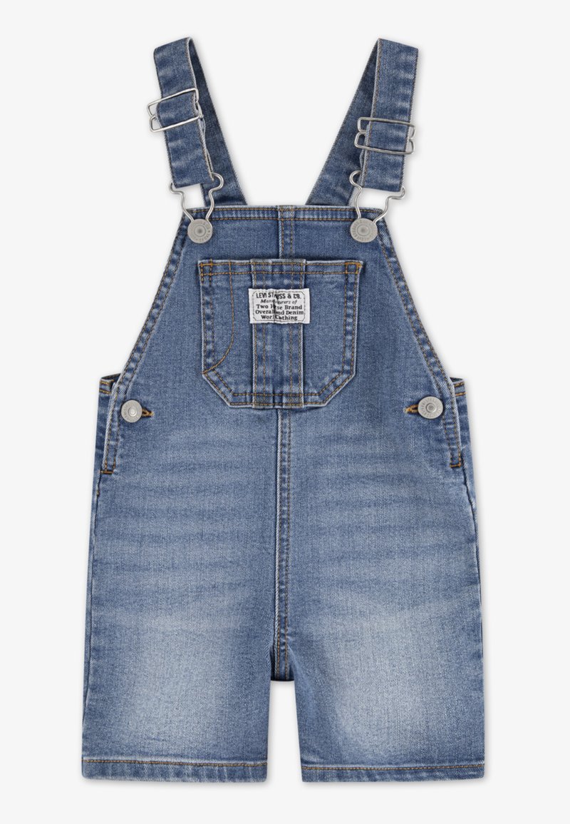 Τζιν σαλοπέτα με ρυθμιζόμενους ιμάντες, μπλε πλύση, με μπροστινή τσέπη και μεταλλικά εξαρτήματα. Φθαρμένες περιοχές προσθέτουν υφή στο ύφασμα.