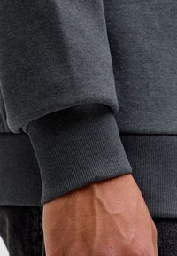 Dunkelgrauer Sweatshirtärmel mit geripptem Bündchen am Handgelenk einer Person, Nahaufnahme.