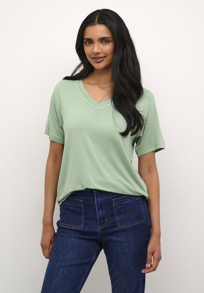 Tricou v-neck de culoare verde mentă, confecționat dintr-un material moale, asortat cu blugi negri cu talie înaltă, având buzunare la spate și cusături vizibile.