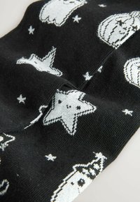 Tejido de punto negro con patrones blancos de estrellas, fantasmas y calabazas, con una superficie texturizada y sutiles acentos metálicos.