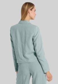 Lichtblauwe, op maat gemaakte blazer met een kraag, rugventilatie en met knopen sluitende manchetten, gemaakt van een gladde stof. Gestyled met bijpassende broek.