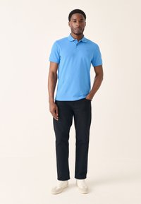 Világoskék rövid ujjú galléros póló egy kis logóval; fekete nadrággal és fehér tornacipővel párosítva.