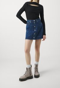 Svart långärmad topp med utskuren detalj på ryggen, kombinerad med en blå jeanskjol med knappar framtill och broderade detaljer. Grå snörkängor.