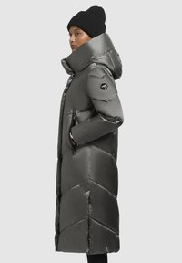 Lång grå pufferjacka med huva, med chevron-vaddering, dragkedjefickor och en logotyp på den övre ärmen. Strukturerad, glänsande yta.