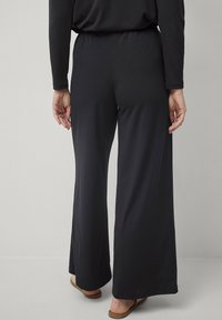 Zwarte, wijde broek gemaakt van zachte stof met een elastische taille. Heeft een gladde textuur en een vloeiende silhouet, geschikt voor casual wear.
