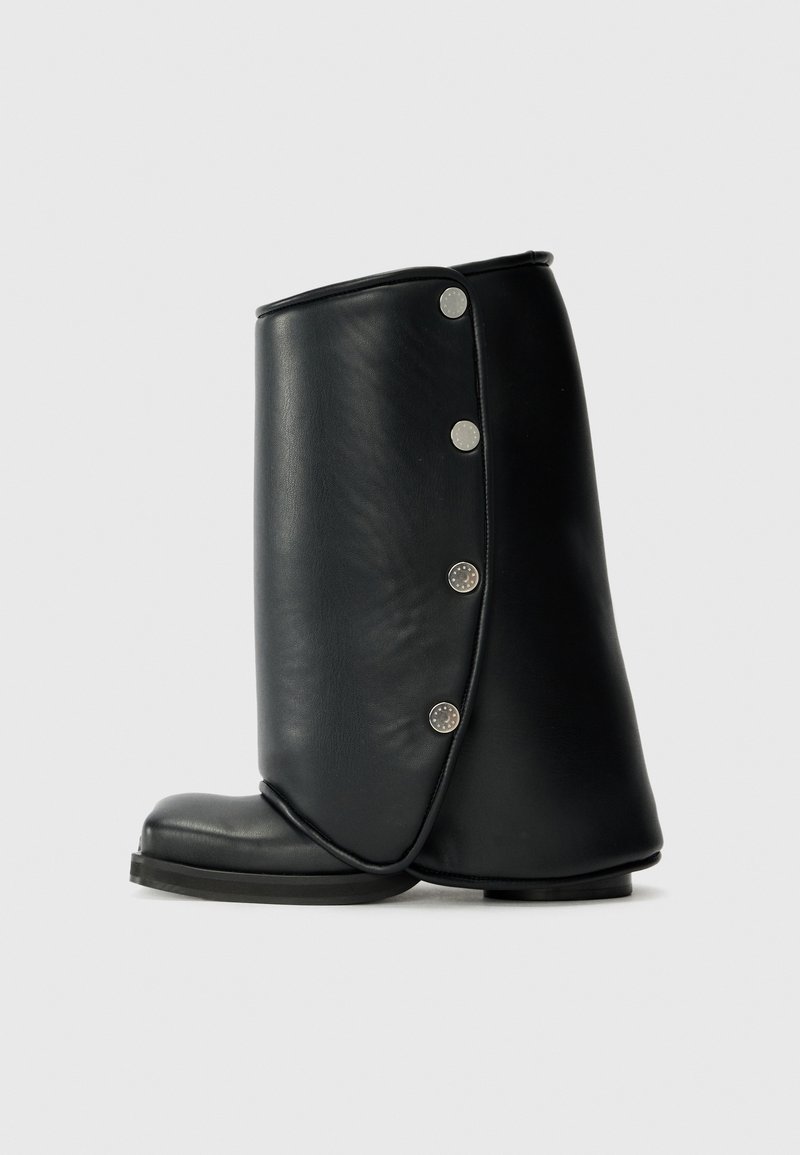 Juodi odiniai kulkšniniai batai su išlenktu dizainu, turintys apvalų pirštą ir dekoratyvinius sidabrinius mygtukus išorinėje pusėje.