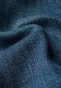 Denim, tkanina o teksturowej i miękkiej strukturze, w ciemnoniebieskim kolorze z klasycznym wzorem skośnym. Powierzchnia ukazuje różne odcienie oraz delikatne plamki.
