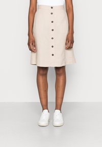 Jupe beige longueur genou en lin avec un design évasé, dotée de fermetures à boutons sur le devant et d'une texture lisse. Assortie à des baskets blanches.