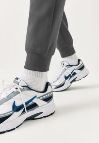 White and navy Nike sneakers with blue accents and gray detailing, paired with gray sweatpants and white crew socks.