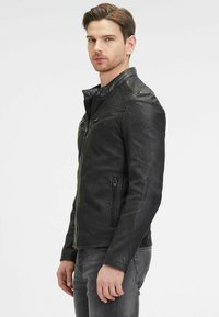 Zwarte leren motorjack met een ritsopening, gestructureerde schouderaccenten en twee zijzakken met rits. Draag het over een zwart shirt en jeans.