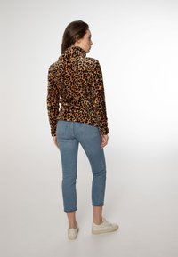 Pullover con stampa leopardata e colletto alto, realizzato in tessuto morbido; abbinato a jeans in denim blu chiaro e sneaker bianche.