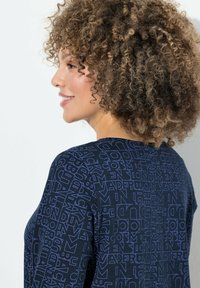 Top navy realizzato in un tessuto testurizzato con un design grafico di varie lettere e forme in azzurro chiaro su tutta la superficie.