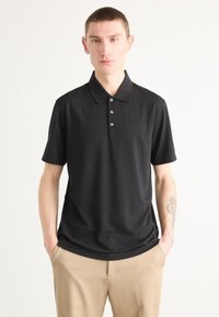 Černé polo tričko vyrobené z hladké látky, s klasickým límcem a tříknoflíkovou légou. Krátké rukávy a uvolněný střih.