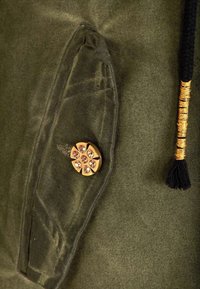 Gros plan sur une poche en tissu vert avec un bouton décoratif doré et un cordon de serrage noir enfilé de fil d'or.