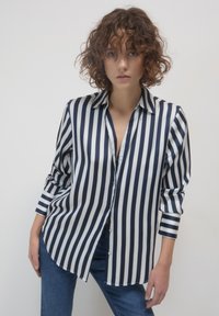 Camicia a righe con bottoni in blu navy e bianco, tessuto lucido, maniche lunghe con polsini a bottone, vestibilità rilassata e orlo arrotondato.