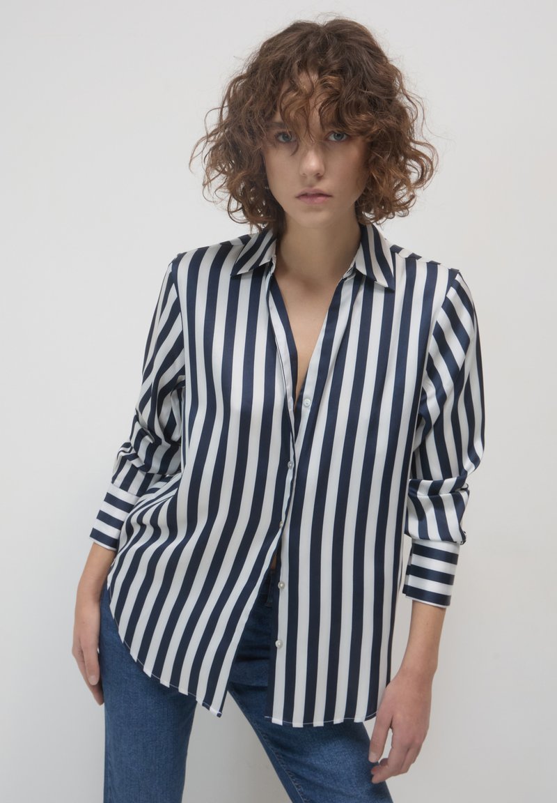 Camicia a righe con bottoni in blu navy e bianco, tessuto lucido, maniche lunghe con polsini a bottone, vestibilità rilassata e orlo arrotondato.