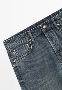 Dark blue denim jeans with a faded finish, five-pocket style, metal button, and copper rivets, featuring a straight cut and subtle texture.