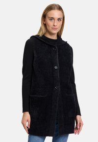 Schwarze gestrickte Weste mit Kapuze, ausgestattet mit Knopfverschl�üssen und zwei Fronttaschen. Weicher Griff, lockerer Schnitt und moderne Silhouette.