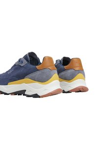 Adidași din suede bleu marine cu accente din piele maro, o talpă intermediară albă și galbenă și o talpă din cauciuc texturată. Au o formă rotundă.