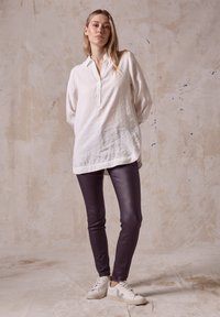 Vit lin skjorta med knapplist, mjuk textur; mörklila tajta byxor; vita sneakers med gröna accenter, minimalistisk design.