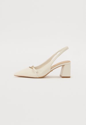 Kremfarvet spids slingback-sko med blokhæl og lille guldbeslag på en ensfarvet hvid baggrund.