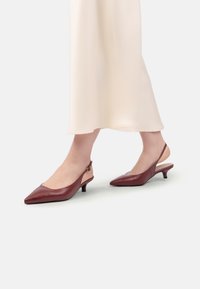 Pantofi cu toc slingback din piele burgundy, cu vârf ascuțit și toc mic, având un panou lateral bej contrastant și breteaua de gleznă ajustabilă.