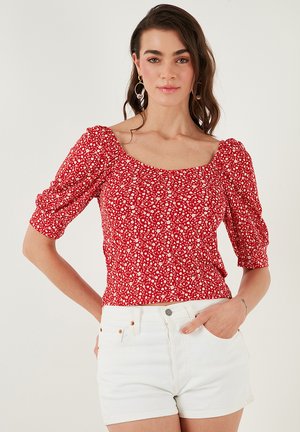Red floral top featuring puff sleeves, a square neckline, and a fitted waist, paired with white denim shorts.
