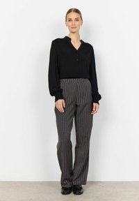 Blusa negra de manga larga con cierre de botones y hombros texturizados, combinada con pantalones grises de rayas finas y zapatos negros.