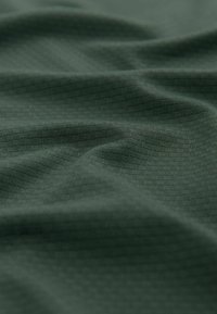 Mørkegrøn tekstureret stof med et subtilt geometrisk mønster og glat fald, der fremhæver dets bløde og fleksible natur.