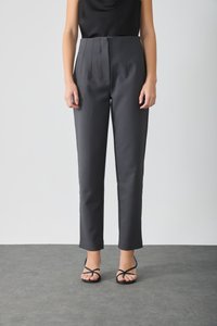 Hochtaillierte, maßgeschneiderte schwarze Hose mit Falten und geraden Beinen. Der Stoff wirkt glatt mit einem leichten Glanz. Tragen Sie sie mit schwarzen Riemchensandalen.
