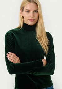 Mörkgrön sammetsturtleneck med långa ärmar. Slät yta, figursydd design, minimalistisk stil och inga synliga mönster eller detaljer.