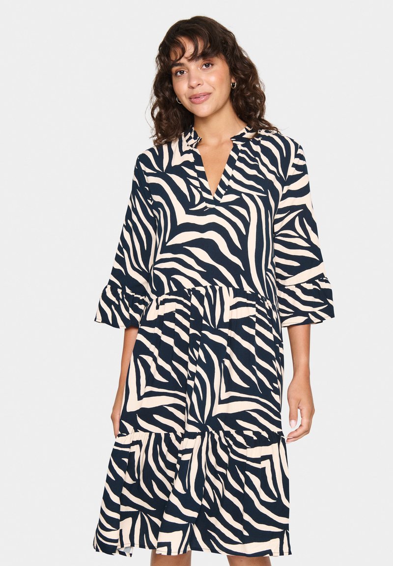 Robe avec un motif zèbre bleu marine et crème, décolleté en V, manches trois-quarts et ourlet en tiers. Fabriquée en tissu léger et fluide.