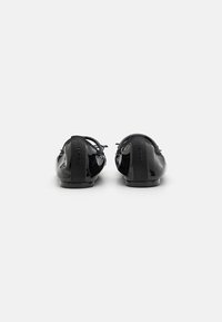 Black patent leather ballet flats with a rounded toe, soft back strap, and minimal heel. Branding on the heel adds detail.