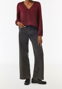 Blusa de satén burdeos con escote en V y mangas largas, combinada con unos vaqueros de mezclilla negros de pierna ancha y cintura alta, y unos zapatos negros tipo slip-on.