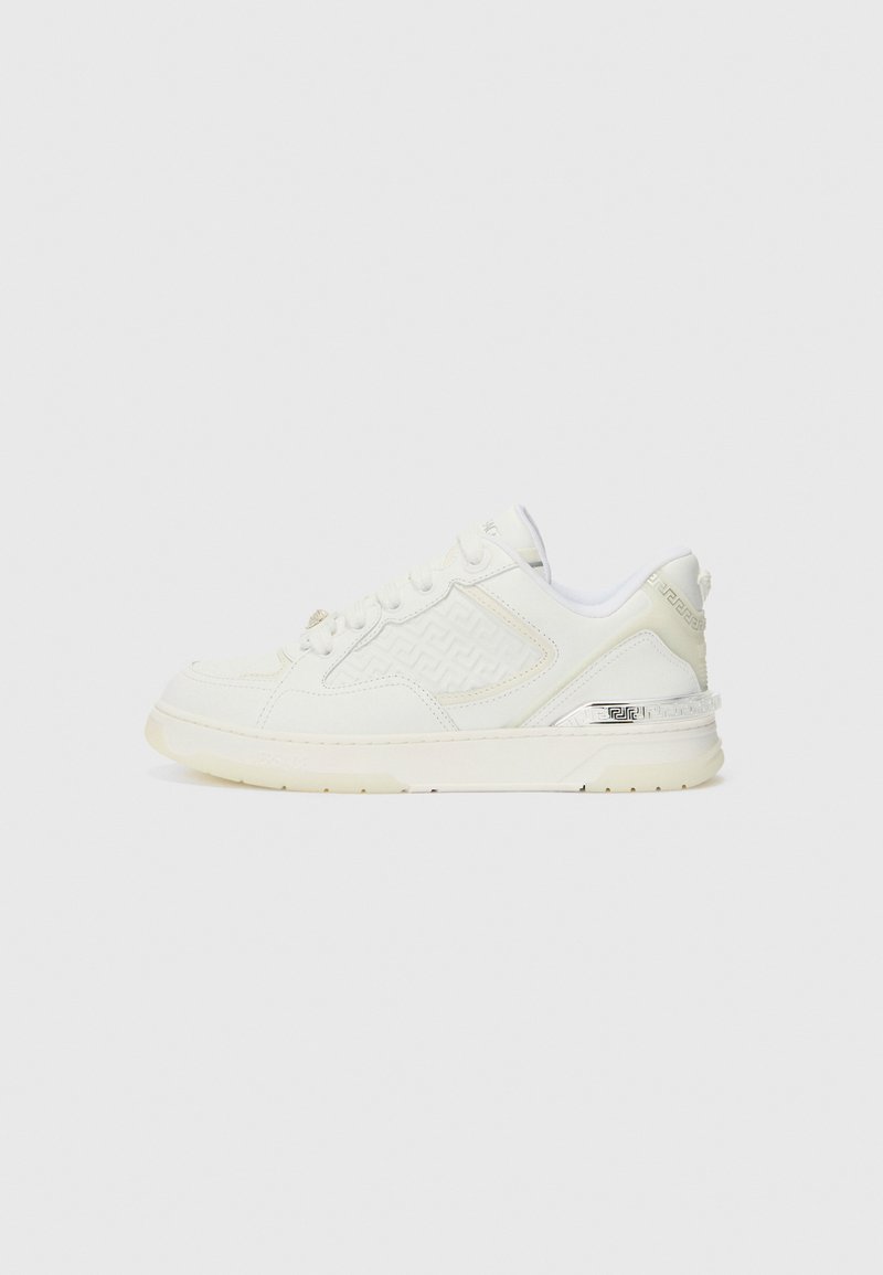 White sneaker featuring a textured side panel, smooth leather upper, and a contrasting silver accent on the heel. Flat rubber sole.