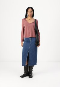Top de manga larga en tono rosa, falda midi de denim con abertura frontal, y botas negras hasta la rodilla con detalles de hebilla. Bolso negro de hombro.