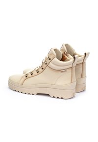 Cream leather ankle boots with gold-toned hardware, padded collar, and textured rubber sole. Features a subtle logo on the side.