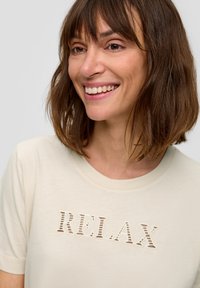 Beige T-Shirt mit ausgeschnittener "RELAX"-Design. Weicher Stoff, kurze Ärmel und ein runder Ausschnitt. Glatte Textur mit lässigem Schnitt.