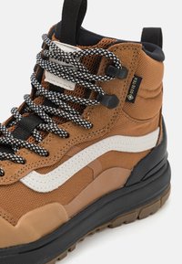 Chaussure de randonnée haute en cuir marron, avec une tige en mesh et en suède, des lacets noir et blanc, une semelle en caoutchouc et une étiquette GORE-TEX pour la résistance aux intempéries.