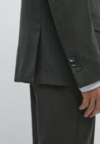 Dunkelgrauer Anzug aus strukturiertem Stoff, mit einer Rückenöffnung und geknöpften Manschetten. Taillierte Passform mit einem sauberen Finish.