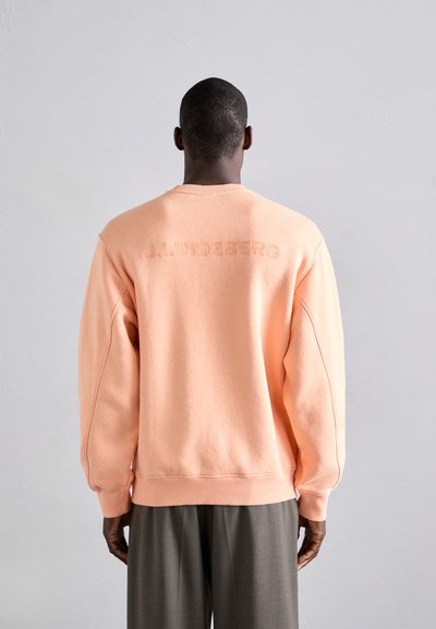 Pfirsichfarbener Pullover mit strukturiertem Finish, eingesetzten Schultern und "J.LINDEBERG" auf der Rückseite geprägt. Rundhalsausschnitt, gerippte Bündchen.