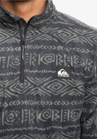 Polarowa bluza w ciemnoszarym kolorze z zielonymi wzorami etnicznymi, z krótkim zamkiem błyskawicznym i naszywką z logo Quiksilver na piersi.