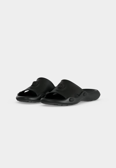 Paire de sandales noires ouvertes à bout ouvert, à enfiler, avec des semelles texturées et un petit emblème sur les brides supérieures, présentées sur fond blanc.