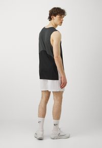 Juoda ir pilka be rankovių sportinė palaidinė, derinama su baltais tinkliniais šortais. Apsirengta su baltomis Nike kojinėmis ir pilkomis sportinėmis batelėmis.