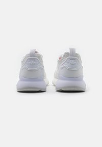 Zapatillas blancas con parte superior de malla, cuello acolchado, diseño minimalista y un logo prominente en la parte posterior. Suela de goma blanda con agarre texturizado.