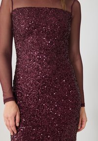 Abito in paillettes bordeaux con un design aderente, caratterizzato da maniche lunghe trasparenti e un colletto quadrato. Le paillettes formano un motivo testurizzato e vorticoso.