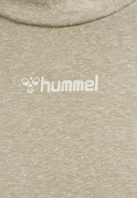 Tissu marron clair texturé avec un logo Hummel blanc et un symbole d'abeille imprimés près d'un col arrondi.