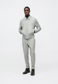 Ανοιχτό γκρι ριγέ σακάκι και παντελόνι με φερμουάρ, συνδυασμένα με μαύρο ζιβάγκο και καφέ μπότακια με κορδόνια.